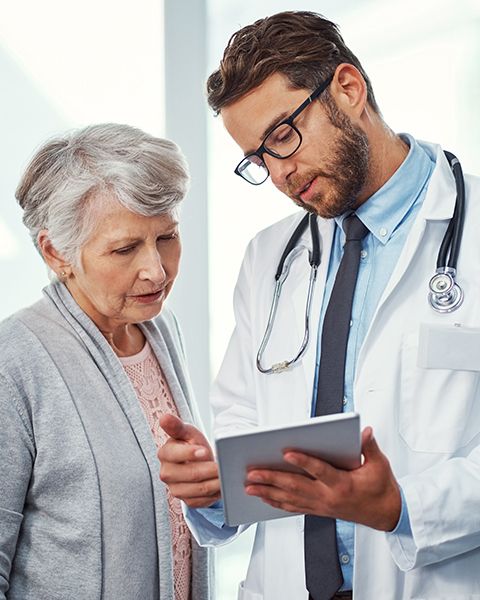 A physician, a white man, using a tablet to discuss medical misinformation worries with a patient, a white senior aged woman.
