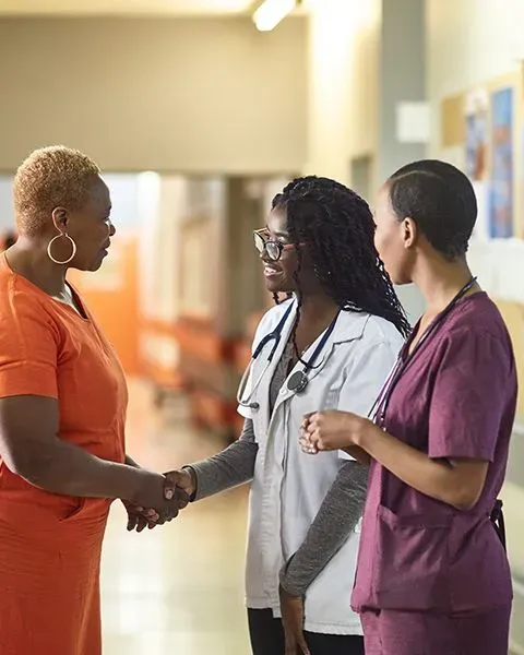 A physician, a black woman, in a white coat and stethoscope meeting her patient, a Black woman (portrait size).