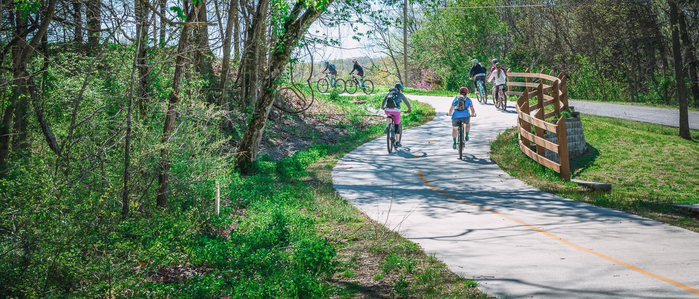 Sunny bike path in Greenville, SC, amid green forest, dedicated for outdoor enthusiasts with bikers.