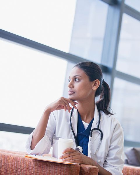 A physician, an Indian woman in a white coat, contemplatively looking out of the medical center window.