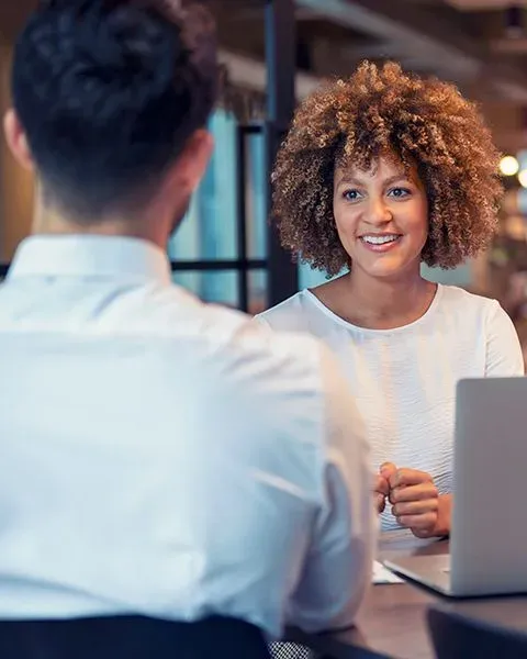 A physician, a Black woman in natural curls, meeting a recruiter to prepare for their site visit, both in business casual.