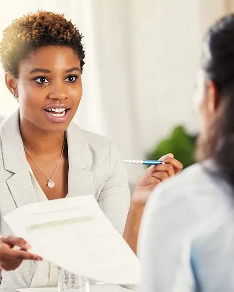 A physician, a Black woman, in short curls and a grey suit jacket, talking to a PS&D recruiter about their curriculum vitae. 