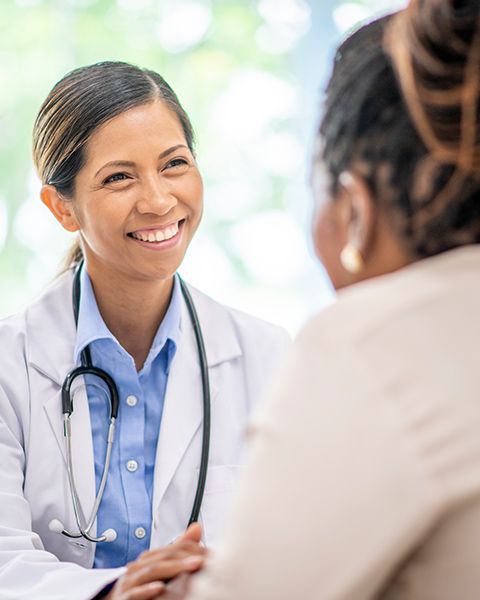 A physician, an Asian woman, in a white coat and stethoscope talking with her patient, a Black woman. 