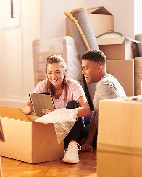 A young couple, a white woman and Black man, are sitting on the floor unpacking moving boxes. 