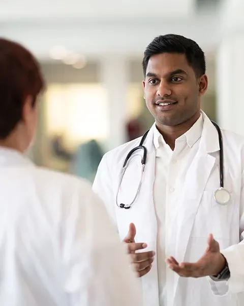 A Medical Resident, an Indian man, smiling and having a positive conversation with an attending physician, a Hispanic woman.