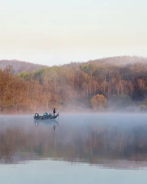 Representing Wisconsin is a view of a foggy river at dusk with a fisherman on a boat in the distance.