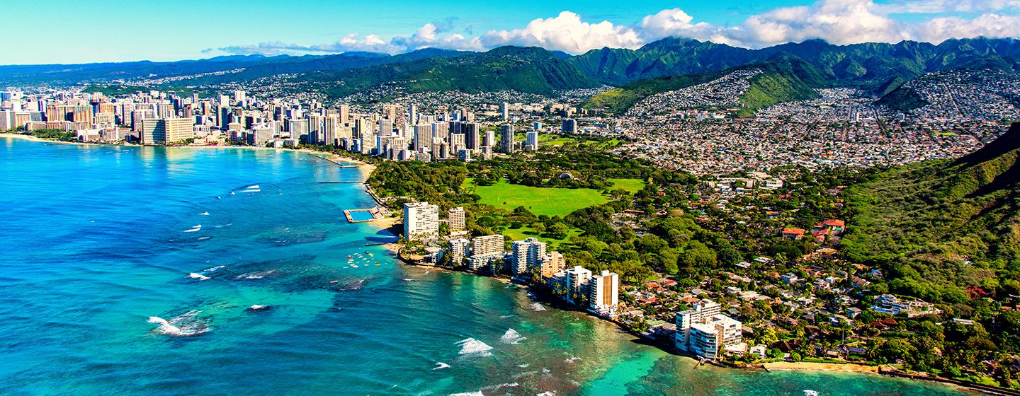 Aerial view of Honolulu, Hawai'i, which is an oceanfront downtown surrounded by green mountains.
