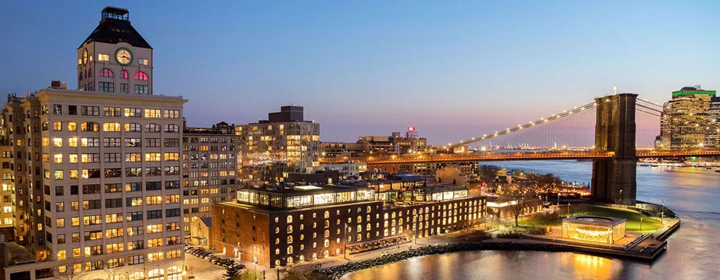 New York City aerial view at night with building and Brooklyn Bridge lights glowing.