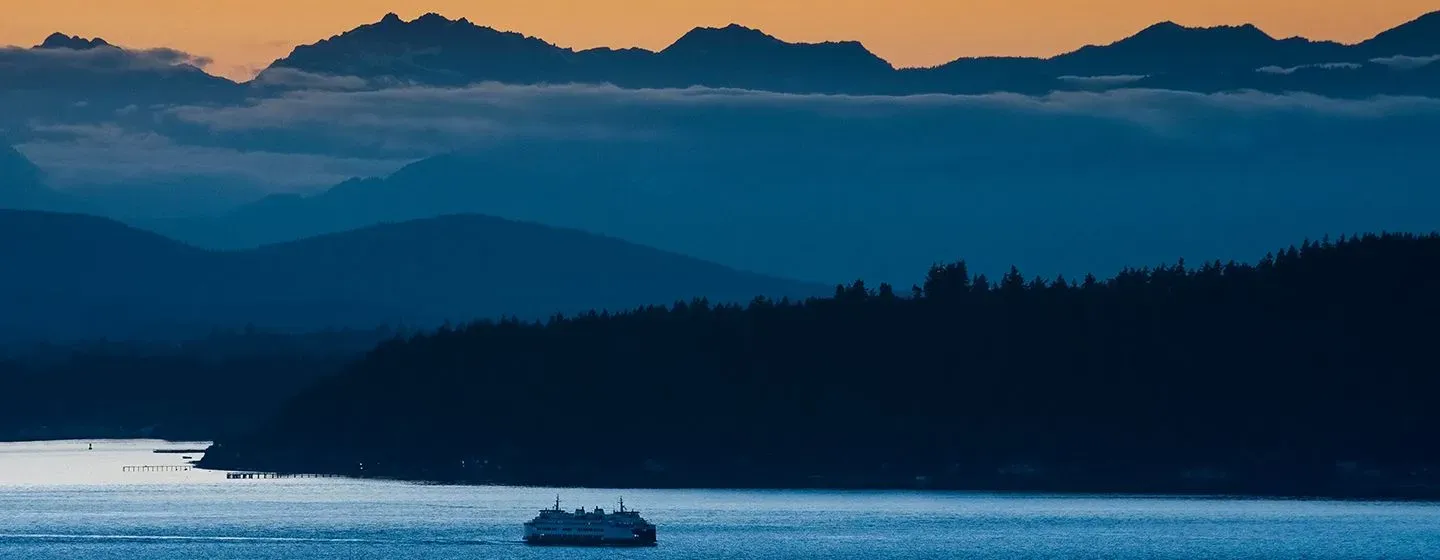 River with boat and in the background hills filled with trees and big clouds in Olympia, Washington.