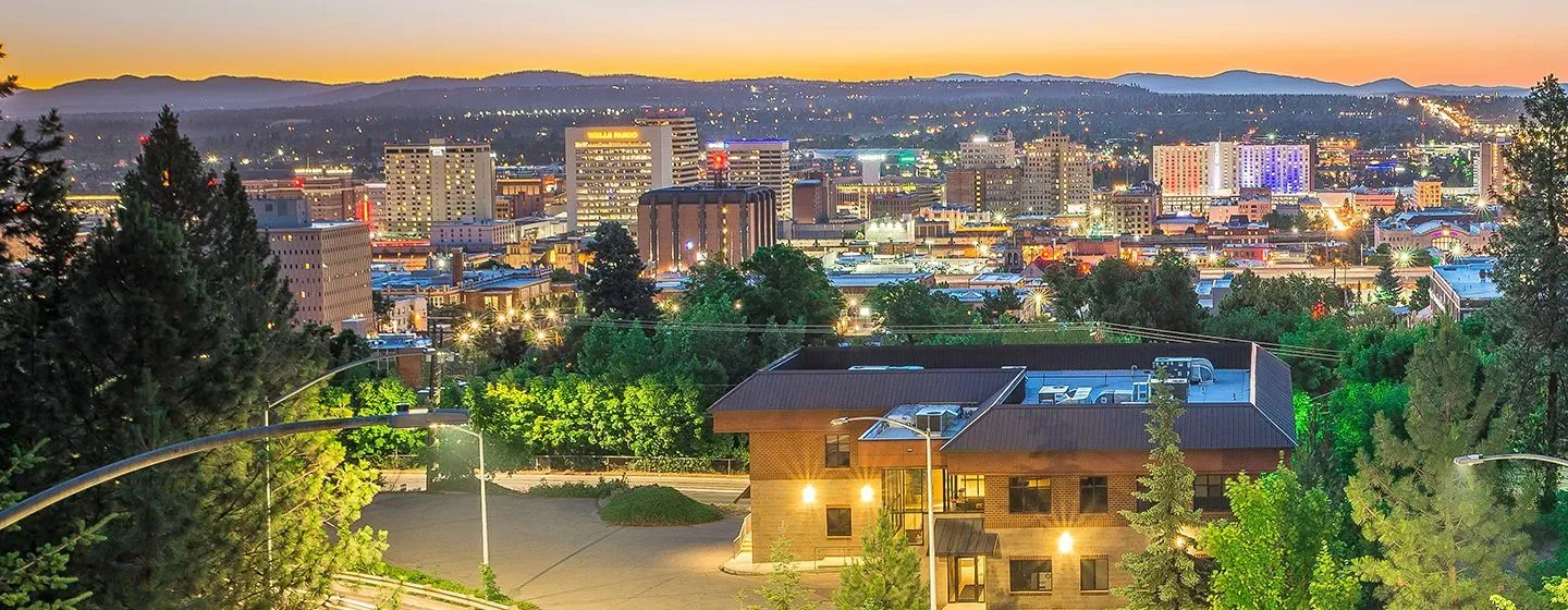 Spokane, Washington skyline view of downtown at sunset with the city lights glowing, buildings surrounded by trees..