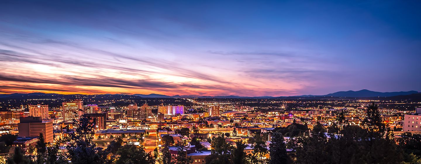 Nighttime skyline aerial view of Spokane, Washington with city lights glowing at sunset.