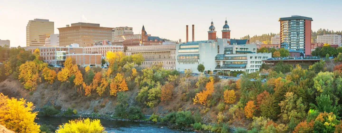 Spokane, Washington skyline view of downtown at sunset with a river surrounded by trees.