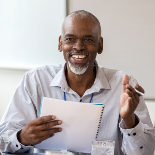 A man with a notebook smiling and leading his team, professionally dressed and smiling, he is Black.