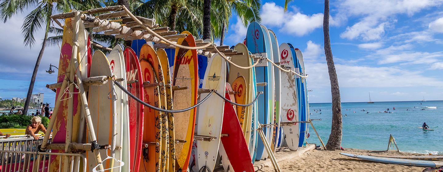 Colorful surfboards stacked and ready to use in front of a sandy beach in Hawai'i.