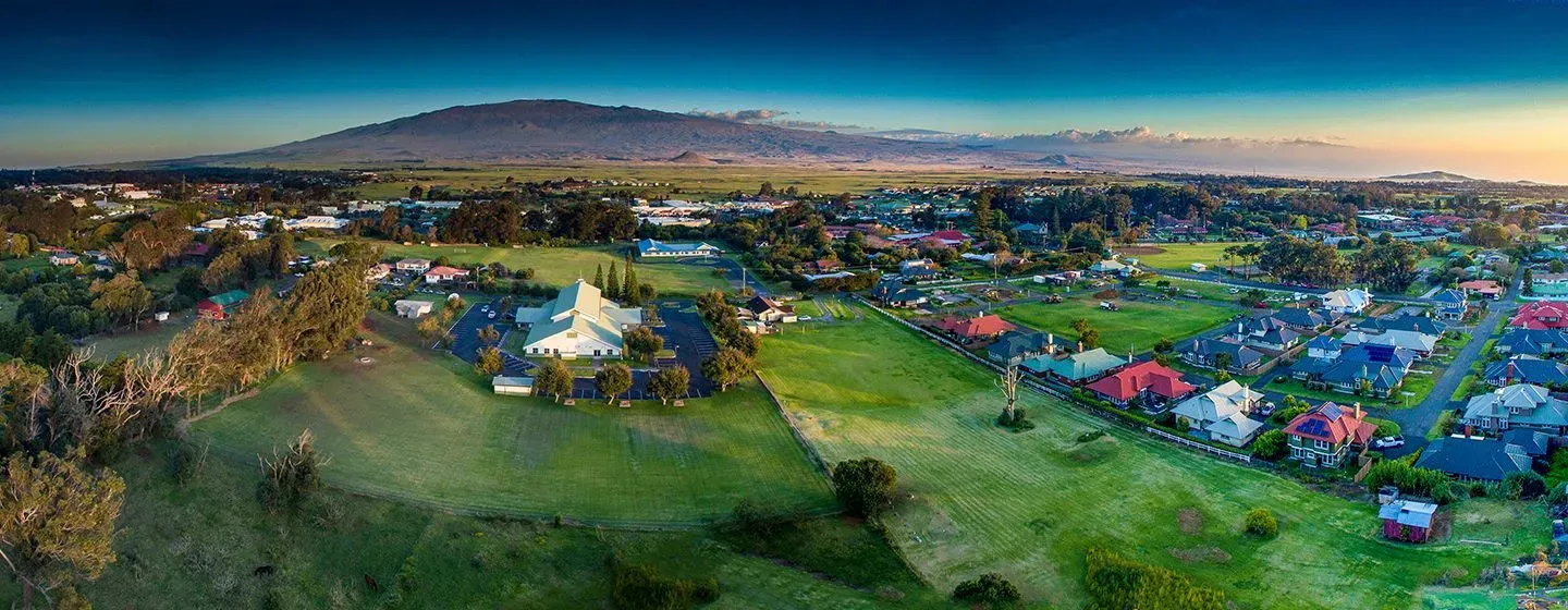 Aerial view a green meadow and colorful homes with a mountain the background in Hawai'i.