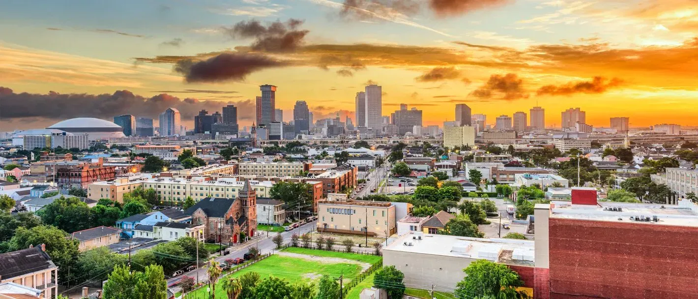 New Orleans skyline at sunset with colorful sky and buildings in the foreground.