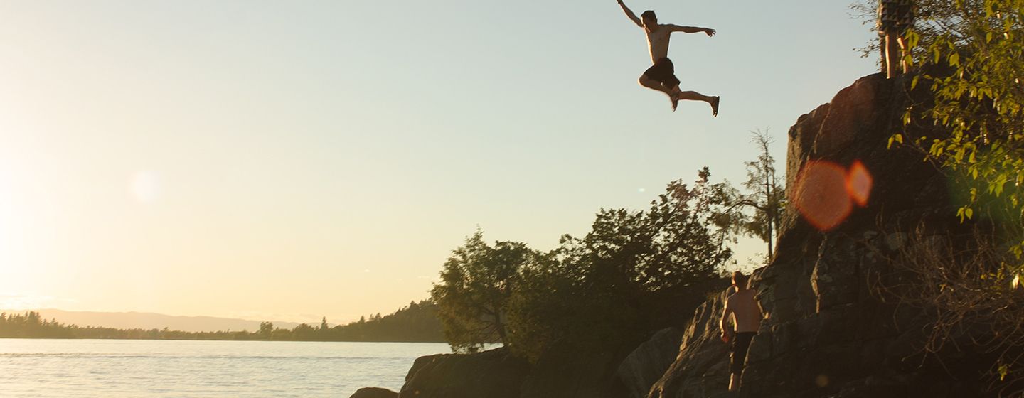 A man jumping off a cliff into the river, at sunset, in the state of Montana.