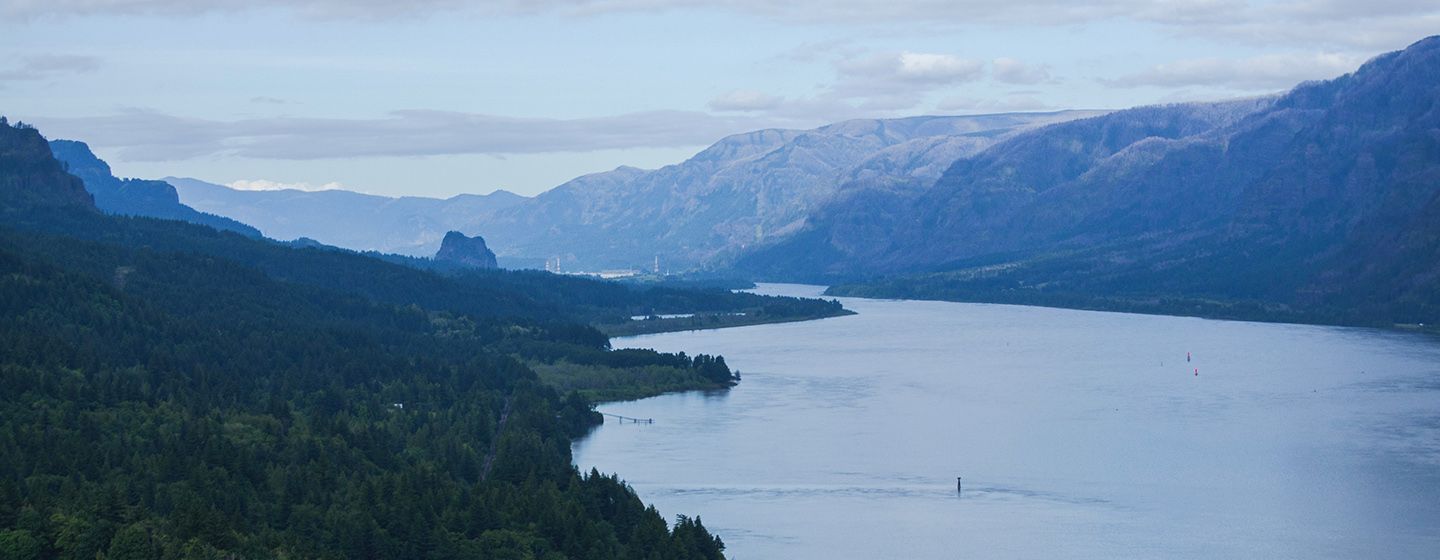 Aerial view of cloudy riverfront with tree filled mountains on both sides in Washington.