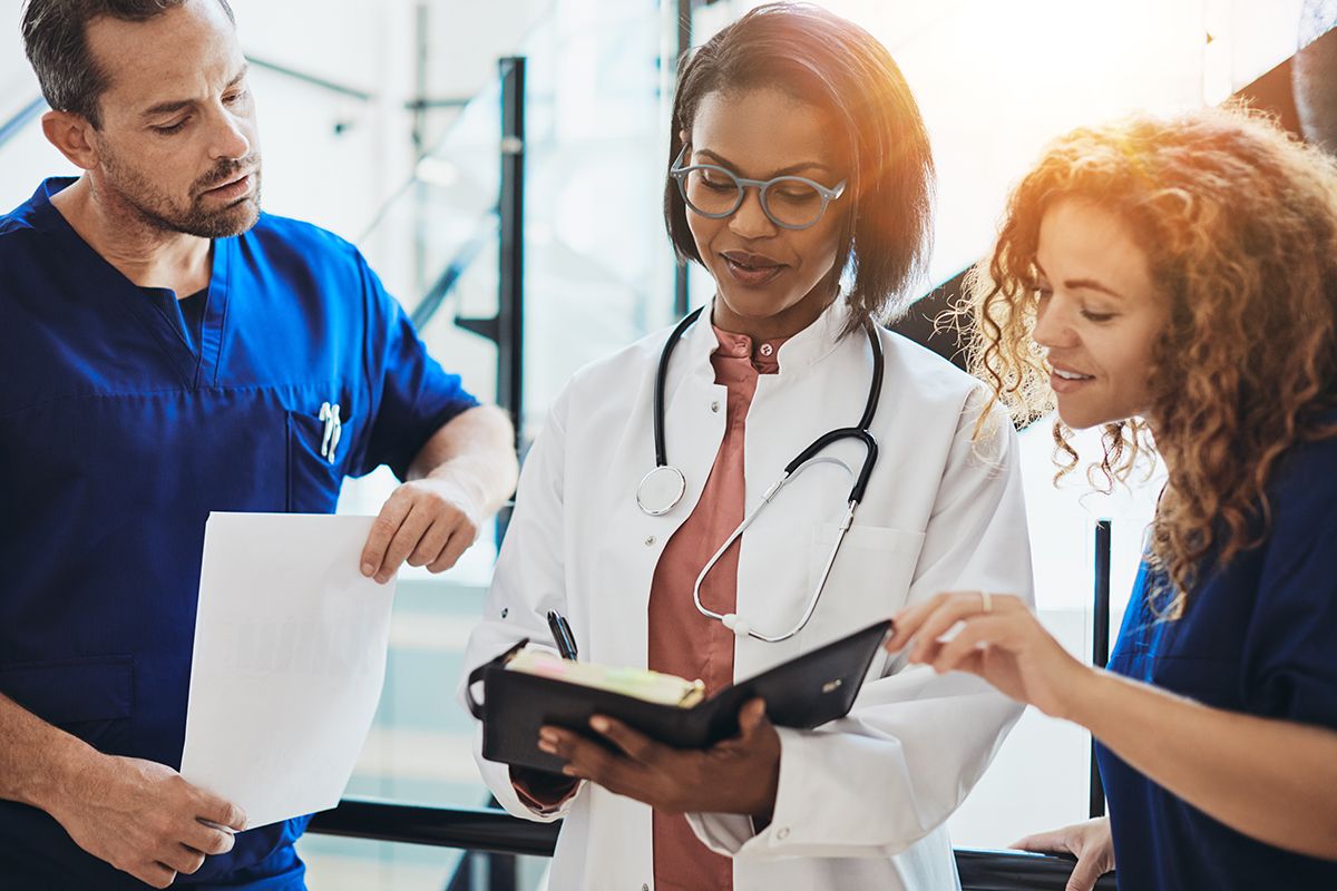 Multigender and multiethnic two women and a man, all physicians, reviewing a patient chart together.