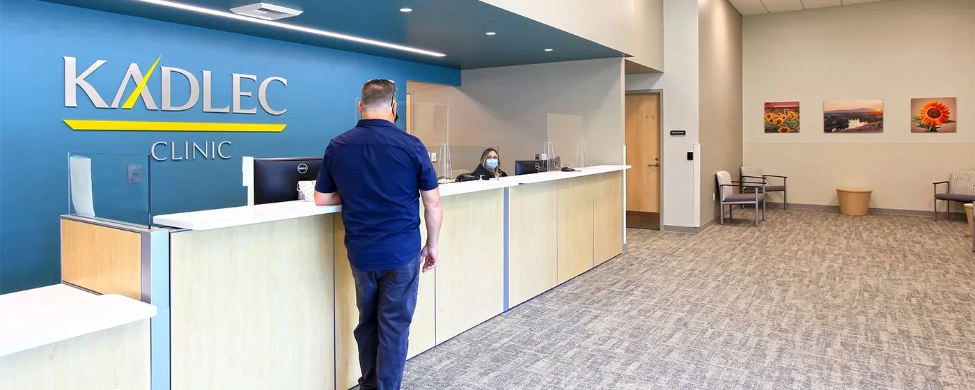 PS&D partner Kadlec's Clinic lobby with a patient, a white man, waiting talking to receptionist at front desk.