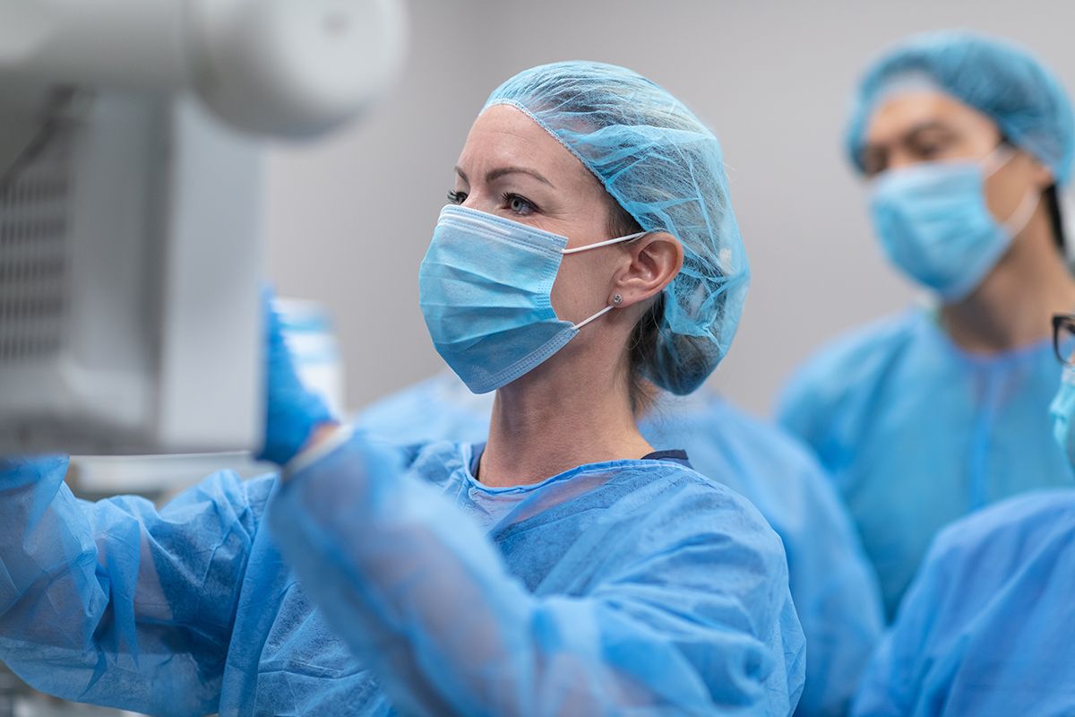 A Cardiologist, a white woman, with her multiethnic surgical team, all in PPE, reviewing a monitor as they prep for surgery.