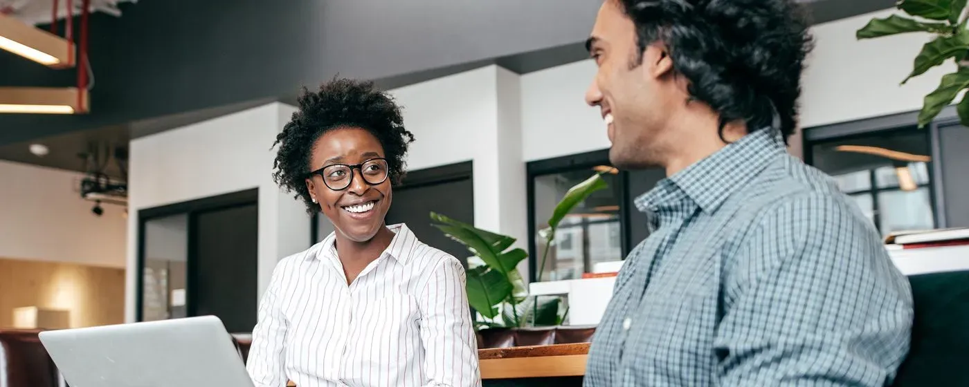 A Gastroenterologist, a Black woman in a professional white top and natural curls, talking with her patient, an Indian man.