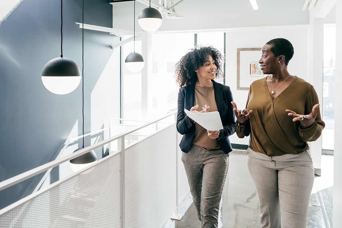 Two Internal Medicine physicians, both Black women professional dressed, one in natural curls the other in waves, walking.