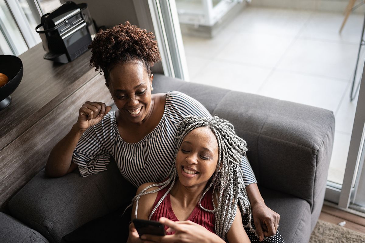 A mother and her daughter, both Black women, watching a funny video on a phone.