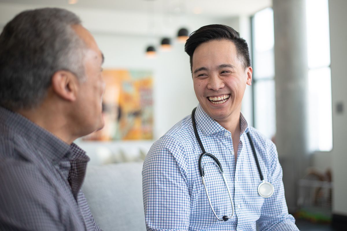 A Gastroenterologist, an Asian man, in a professional top and stethoscope talking with his patient, a Black older man.