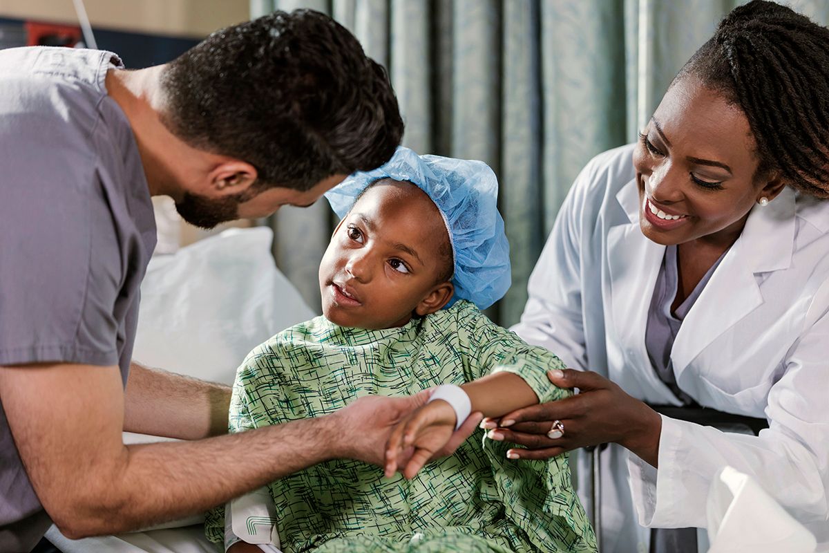 A Pediatric physician, a Black woman, in a white coat, with her patient, a young Black boy, next to him a nurse, a Black man.