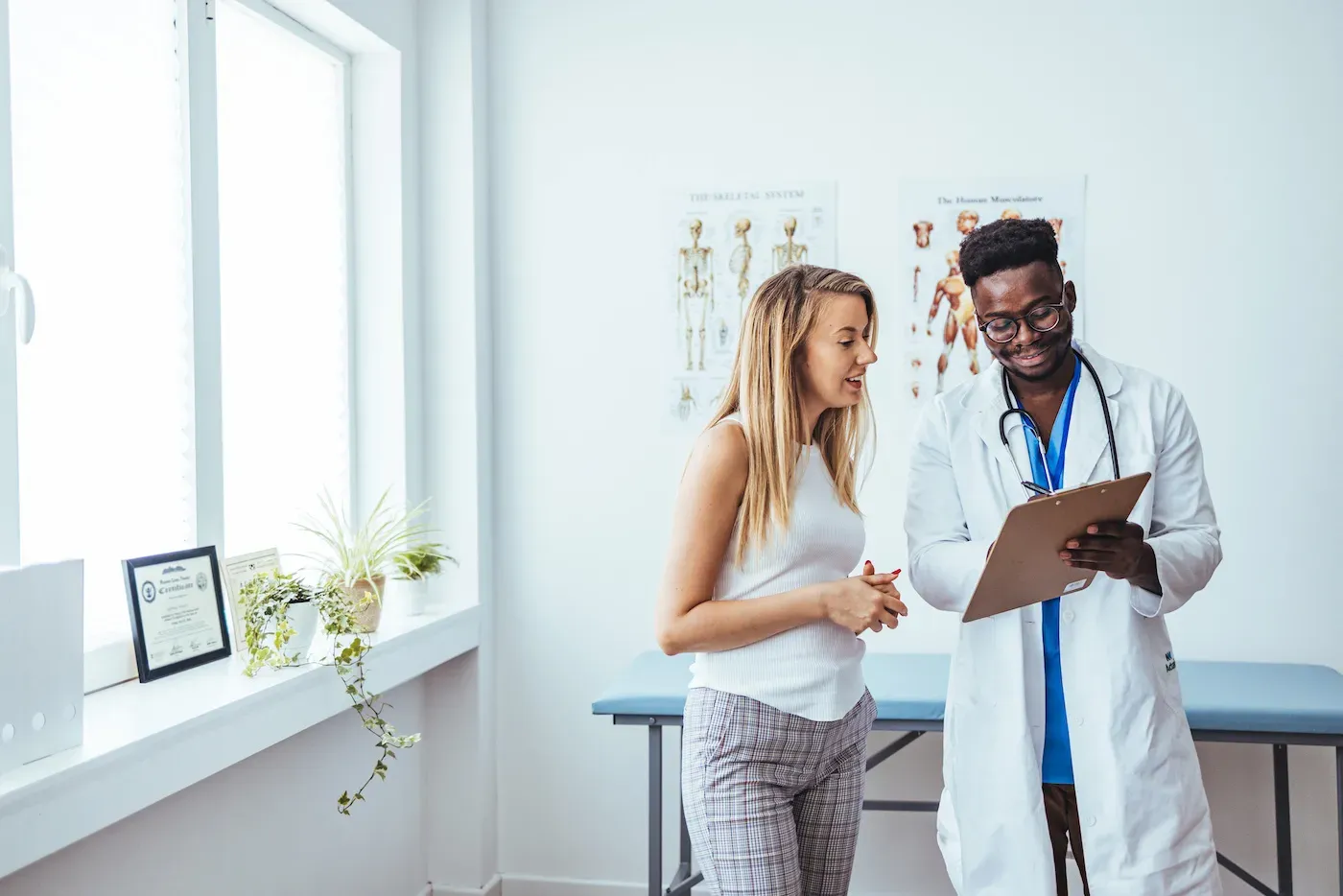 A male doctor in a white lab coat is showing a female patient something on a clipboard while they talk.