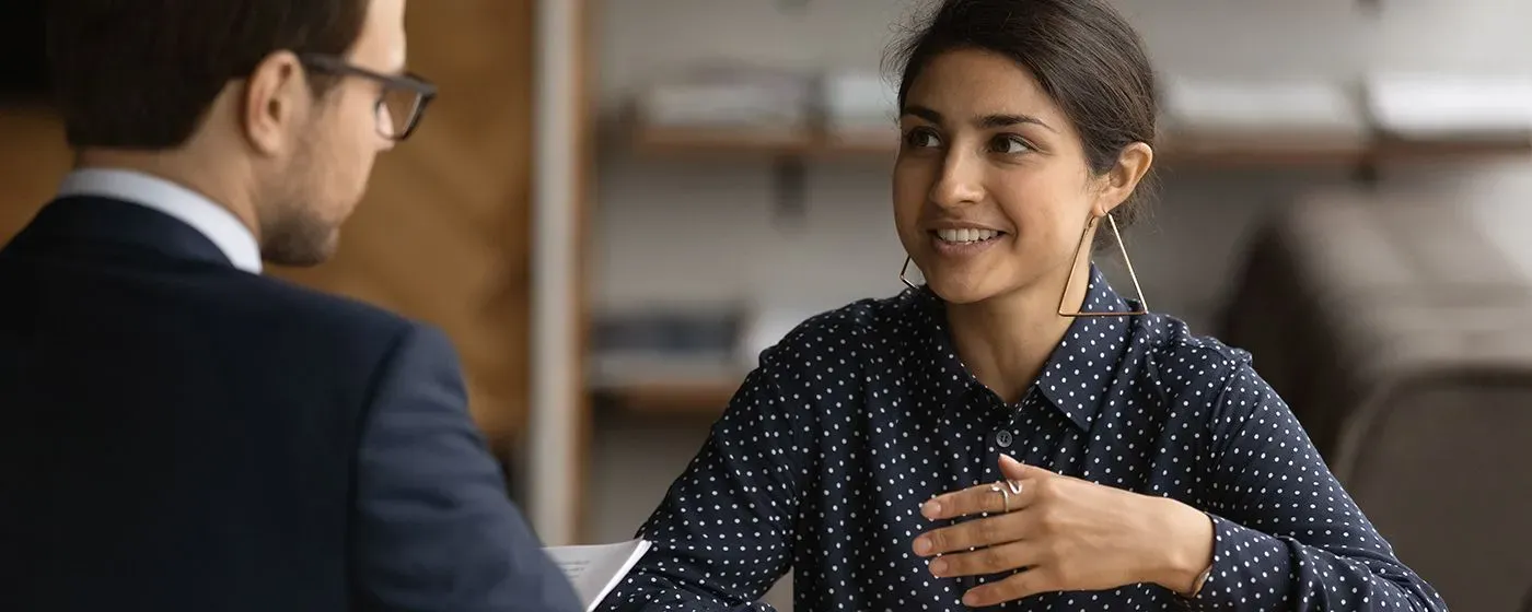 A PS&D recruiter, a white man, listening to a Psychiatrist, a young and trendy Middle Eastern woman, share her career goals.