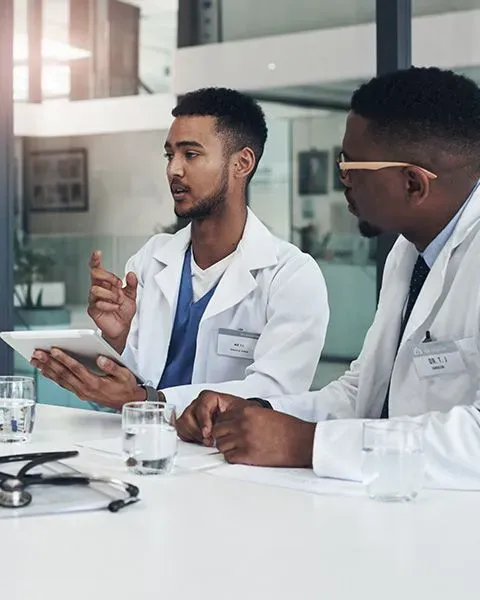 A medical resident, consulting with another physician about a patient, both are Black young men.